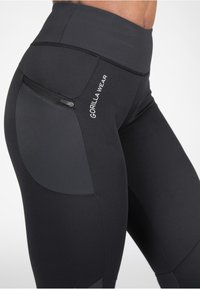 Zwarte legging met een hoge tailleband, voorzien van gestructureerde zijpanelen en een ritszakje, gebrandmerkt met "GORILLA WEAR" in het wit.