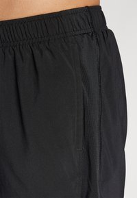 Black shorts made of lightweight fabric with an elastic waistband. Features side pockets and a smooth texture. Simple, functional design.