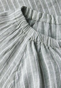 Gros plan sur un tissu gris avec des tailles élastiques, présentant des rayures blanches verticales et un matériau tissé texturé.