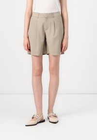 Khaki šortky s uvolněným střihem, sklady na přední straně a bočními kapsami. Vybavené světle růžovými plochými botami se strapcem a přezkou.