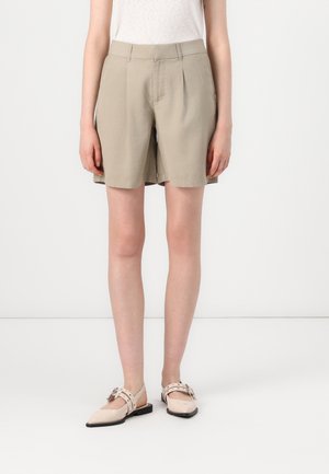 Shorts khaki à coupe décontractée, avec une devant plissé et des poches latérales. Associés à des chaussures plates rose pâle avec une sangle et un détail de boucle.