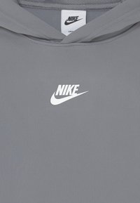 Šedá mikina Nike s tkáňovou strukturou, s bílým logem na hrudi. Kapuce a těsné uchycení.