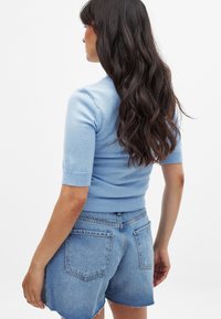 Šviesiai mėlynas raukšlėtas trumpo rankovės marškinėliai, derinami su aukštuoju liemeniu džinsiniais šortais, turinčiais suplėšytus kraštus ir dvi nugarines kišenes.