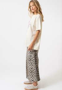 T-shirt en coton crème à manches courtes avec un motif violet, associé à une jupe imprimée léopard et des baskets de couleur claire.