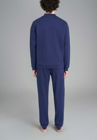 Felpa blu navy a maniche lunghe con colletto rotondo e pantaloni abbinati. Il tessuto sembra morbido, con una consistenza liscia e senza motivi visibili.