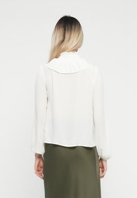 White blouse with a large, structured collar, long sleeves, and a sheer texture. The hem is slightly cropped, revealing an olive skirt underneath.