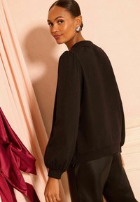 Blusa negra de manga larga con cuello redondo y hombros abullonados. Tejido suave, combinada con pantalones de cuero negro brillante.