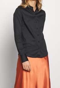 Svart långärmad skjorta med knappar, slät tyg, skräddarsydd passform, spetskrage, med svarta knappar och kontrasterande manschettdetalj.