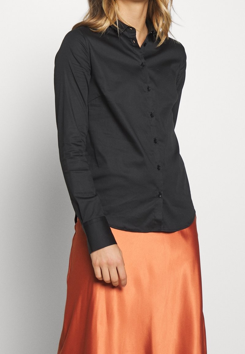 Svart långärmad skjorta med knappar, slät tyg, skräddarsydd passform, spetskrage, med svarta knappar och kontrasterande manschettdetalj.