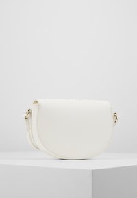 Bílá kožená kabelka přes rameno s obloukovým tvarem, minimalistikým designem a zlatým zapínáním. Hladká textura s jemnými detaily šití.