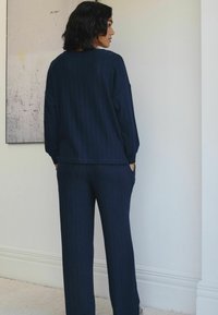 Dunkelblaues geripptes Outfit mit lockerer Passform, bestehend aus einem Langarmoberteil und passenden Hosen, beide mit Seitentaschen und strukturierter Oberfläche.