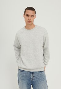 Lys grå genser med rund hals, ribbe cuffs og hem. Laget av et mykt stoff, med en avslappet passform. Brukt sammen med blå jeans.