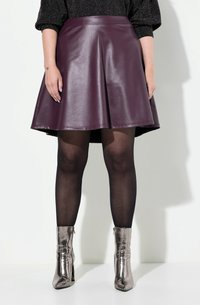 Une jupe évasée en simili cuir bourgogne à taille haute, associée à des collants noirs et des bottes métalliques mi-mollet avec fermeture éclair.