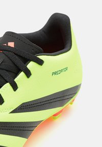 Botín de fútbol verde lima con acentos negros, que presenta una superficie texturizada, cordones negros y la palabra "PREDATOR" en verde en el lateral.