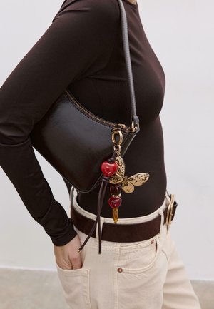 Black leather handbag with a curved shape, gold hardware, and a decorative charm featuring a butterfly, heart, and colored beads.