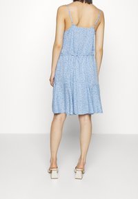 Ljusblå klänning med tunna axelband, mönstrad textur i vitt, knälång, avslappnad passform, har ett lagerdesign, kombinerad med klacksandaler.