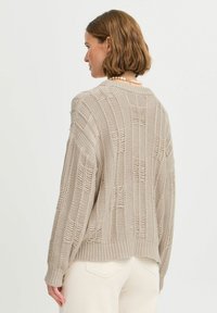 Pull en maille beige clair avec une coupe décontractée, présentant un motif texturé de rayures verticales et des poignets et un ourlet côtes.