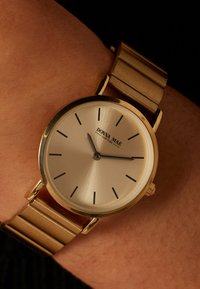 Gold-tone wristwatch with a silver dial, minimalist black hour markers, and a textured metal band featuring flat links. Brand: Donna Mae.