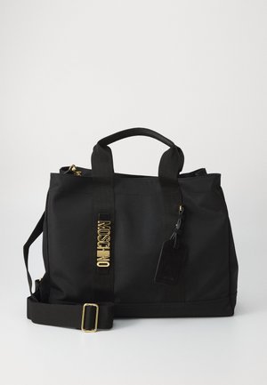 Borsa a tote nera Moschino con doppi manici, tracolla regolabile, scritta in oro e etichetta bagaglio nera attaccata su sfondo semplice.