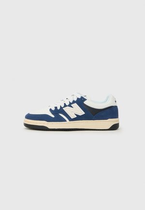 Low-top athletic sneaker in white and navy blue with beige sole, white laces, and a large "N" logo on the side.