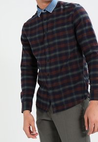 Flanellen overhemd in donker marineblauw, bordeauxrood en groene ruit met een lichte denim kraag. Kenmerken zijn knoopsluitingen en lange mouwen. Gestructureerde stof.