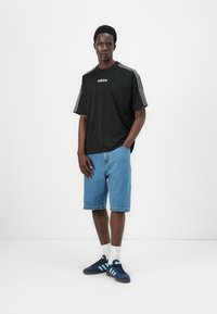 Fekete, rövid ujjú póló fehér Adidas logóval, világoskék farmer rövidnadrággal párosítva, valamint sötétkék sportcipő világoskék csíkokkal.