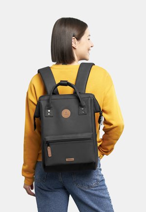 Schwarzer Nylon-Rucksack mit zwei Schultergurten, vorderer Reißverschlusstasche und einem oberen Griff. Verfügt über ein rundes Logo und Lederakzente.