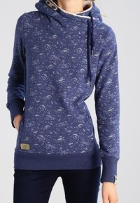 Granatowa bluza z kapturem z fakturowanym wzorem fal i ryb. Posiada kołnierz z kapturem, ściągacz ze sznurkiem i ściągacze na mankietach oraz dole. Miękkie wnętrze.