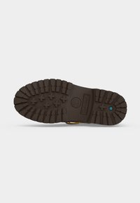 Σόλα καφέ μπότας Timberland με βαθιά πέλματα, σχέδια σε σχήμα σταυρού και ένα μικρό μπλε εξάγωνο κοντά στη φτέρνα.