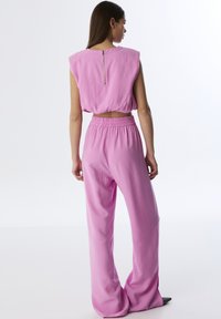 Růžový cropped top s širokým ramenem a zipem na zadní straně, doplněný o volné kalhoty s elastickým pasem ve stejném odstínu.