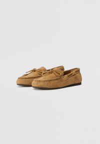 Brown suede moccasin-style shoes featuring a rounded toe, decorative laces, a stitched upper, and gold-tone hardware accents.