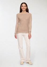 Beżowy sweter dzianinowy o wzorze teksturowym, z okrągłym dekoltem i długimi rękawami, w połączeniu z białymi spodniami dzwonami i jasnymi butami.