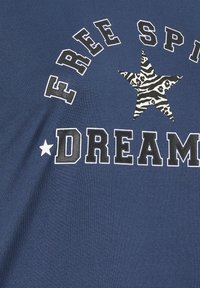 Mörkblå T-shirt med vit text som säger "FRIA ANDAN" och "DRÖMMARE," med en stor stjärndesign i zebramönster och leopardmönster.