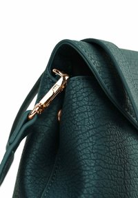 Zelená texturovaná kožená kabelka s zakřiveným designem, vybavená kovovým uzávěrem v růžově zlaté barvě a rukojetí. Detailní záběr na popruh a kovové části.