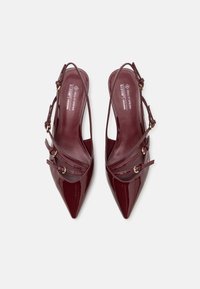 Burgundy kein nahkatossut, joissa on terävä kärki ja useita teksturoituja hihnoja, sekä kultaiset koristeet. Vegaaninen muotoilu.