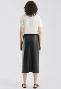 Czarna skórzana spódnica midi z tylnymi kieszeniami, gładką fakturą i dopasowanym fasonem, zestawiona z prostym białym t-shirtem i płaskimi sandałami.