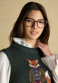 Adīta bez piedurknēm džemperis tumši zaļā krāsā ar lapsas izšuvumu, apvienots ar baltu kreklu ar apkakli, kas rotāta ar mežģīņu detaļām.