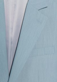 Giacca di abito azzurro chiaro con tessuto testurizzato, rever a punta e taschino sul petto. L'interno presenta una fodera a righe contrastanti.