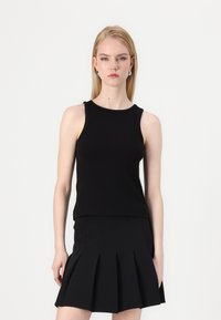 Black ribbed tank top with a round neckline, relaxed fit, paired with a black pleated mini skirt featuring multiple sharp pleats.