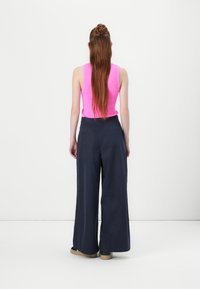 Navy weite Hosen mit hoher Taille, kombiniert mit einem figurbetonten rosa Tanktop. Der Stoff wirkt glatt und hat einen eleganten Fall.