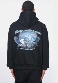 Zwarte hoodie met een grafische print van twee vogels die vliegen tegen een bergachtig landschap, met de tekst "Bring me the horizon" erboven.