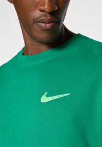 Green cotton T-shirt with a round neckline and short sleeves. Features a prominent white Nike logo on the chest. Smooth texture.