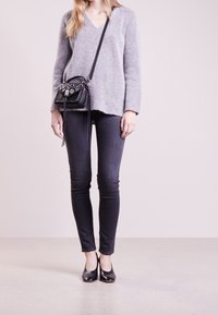 Szary sweter z wełny z dekoltem w serek, czarna skórzana torebka na ramię z detalami metalowymi, ciemne dżinsy i czarne szpilki.