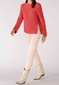 Pull en corail à côtes avec des manches larges, fentes sur les côtés, assorti à un jean fitted rose clair et des bottes de cowboy en cuir blanches.