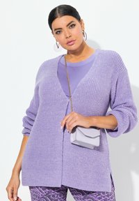 Lila stickad cardigan med v-ringning, sänkta axlar och långa ärmar. Bärs över en matchande topp, ihop med en liten lila handväska.