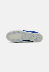 Scarpa da atletica blu con una parte superiore in tessuto testurizzato e una suola in gomma bianca con un motivo esagonale. Dettagli verdi visibili vicino al tallone.