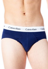 Slip in cotone blu navy con elastico bianco riportante la scritta "Calvin Klein" in lettere nere. Texture liscia, design classico dello slip.