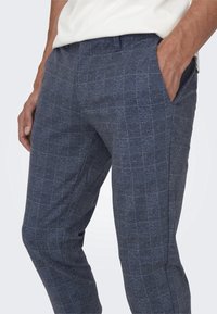 Pantalons à motifs bleu marine avec un design à carreaux. Fabriqués en tissu texturé, comportant deux poches latérales et une coupe ajustée.