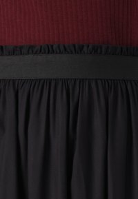 Zwarte rok met geplooide textuur, met een brede, horizontale zwarte tailleband. De top is burgundy met een geribbeld patroon.