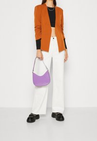 Oranžový blazer, černý crop top, bílé široké kalhoty, černé platformy a malá fialová kabelka. Jednoduchý stříbrný řetízek jako akcent.